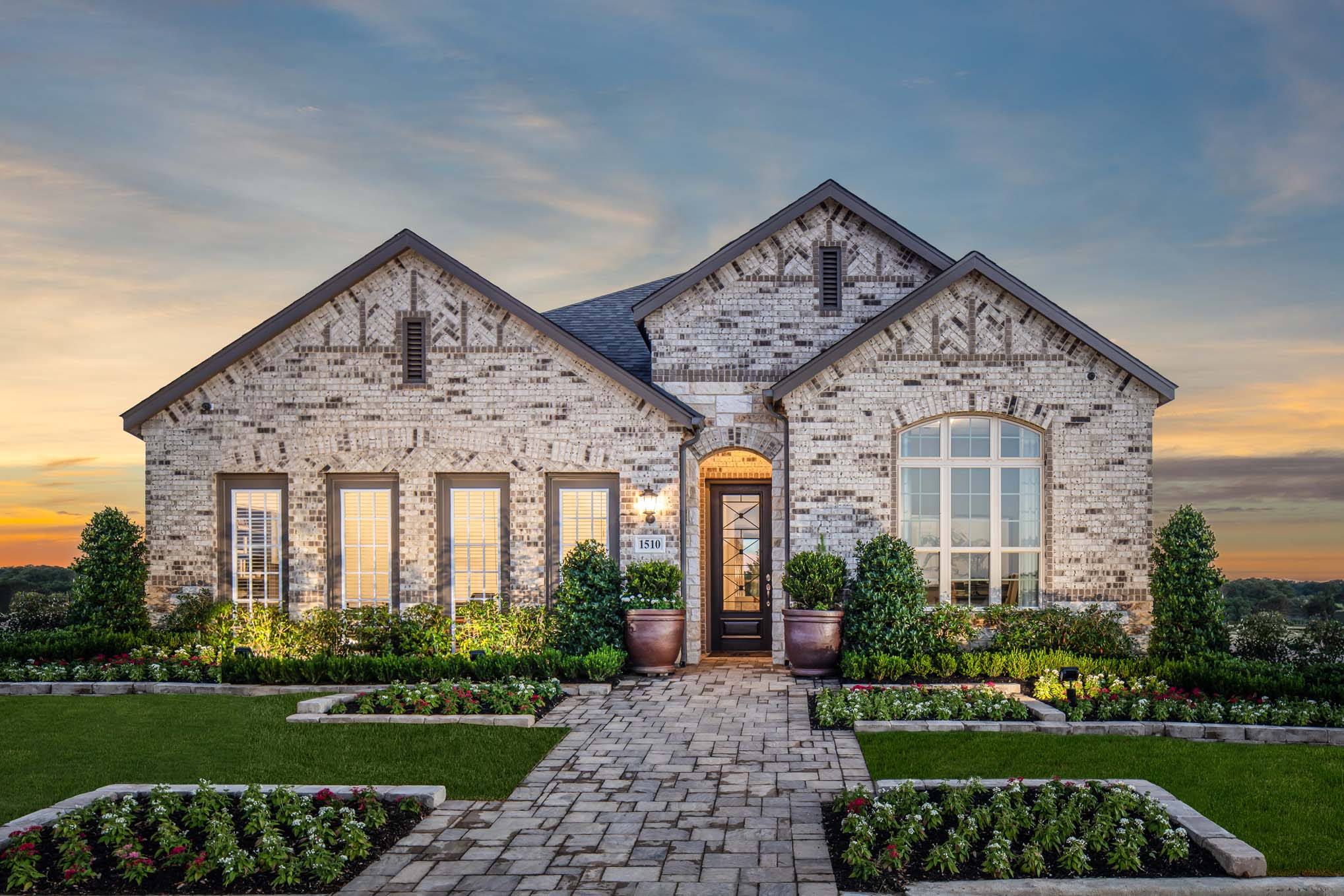 Exterior shot of Meyer Ranch custom home with natural stone facade and manicured garden against sunset backdrop
