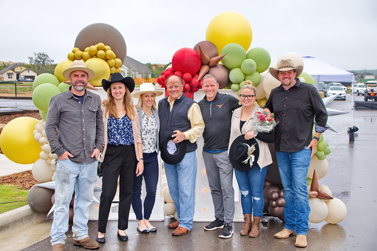 Group posing for photos in cowboy hats at the Meyer Ranch model home park opening event