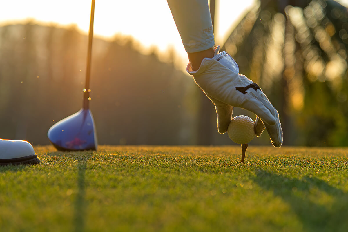 Man wearing golf glove setting golf ball on tee