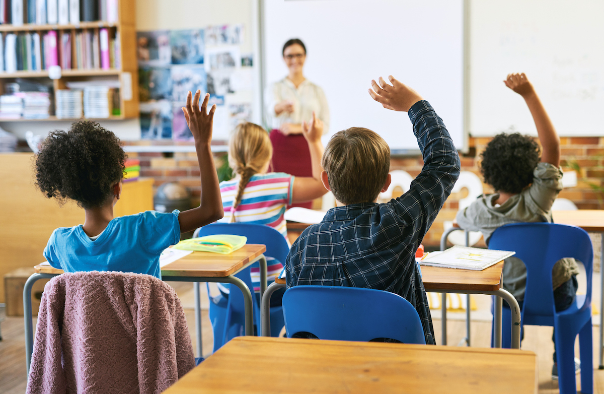 Shot of an unrecognizable group of children sitting in their school classroom and raising their hands to answer a question