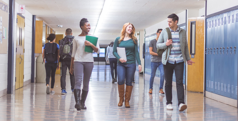 Three students walking down a school hallway talking to each other. 